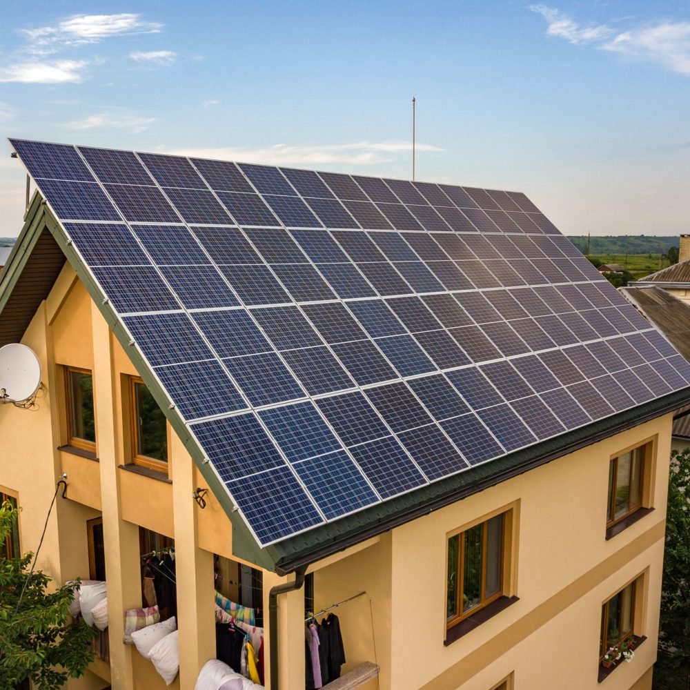 Aerial top view of new modern residential house cottage with blue shiny solar photo voltaic panels system on roof. Renewable ecological green energy production concept.